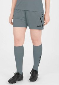 Pantaloni corti sportivi grigi con logo nero, caratterizzati da una striscia laterale e dettagli con bottoni. Abbinati a calze grigie al ginocchio e scarpe da calcio nere.