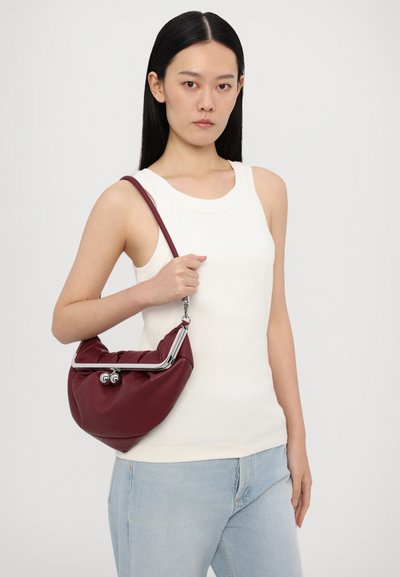 Burgunderfarget lærhåndveske med rynket design og sølvfarget maskinvare. Vesken har en buet topp og en kjede-reim. Modellen har på seg en hvit tanktop.