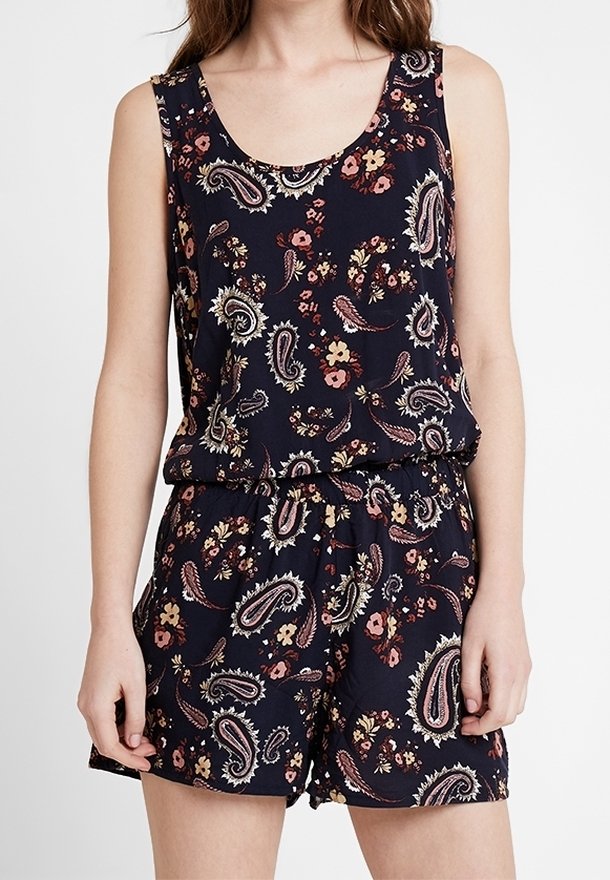 Combinaison bleu marine sans manches avec motifs cachemire roses et beiges et motifs floraux, taille élastique, portée par une personne debout, les bras détendus.