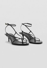 Schwarze Riemchensandalen mit niedriger Absatzhöhe. Hergestellt aus glattem Material, mit dünnen Riemen und einem eleganten Fußbett-Design. Schlicht und elegant.