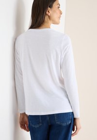 Hvid langærmet skjorte med rund halsudskæring og glat tekstur, parret med blå denim jeans med et klassisk lomme-design.