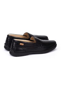 Zapatos negros de cuero tipo slip-on con un diseño cosido, parte superior texturizada, forro suave y suela de goma. Presenta una pequeña etiqueta con el logo en el costado.
