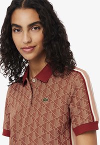 Rode polo shirt met een gekrulde kraag, ribbelmouwen en een groene geborduurde logo. Heeft een geometrisch ontwerp en contrasterende zijstrepen.