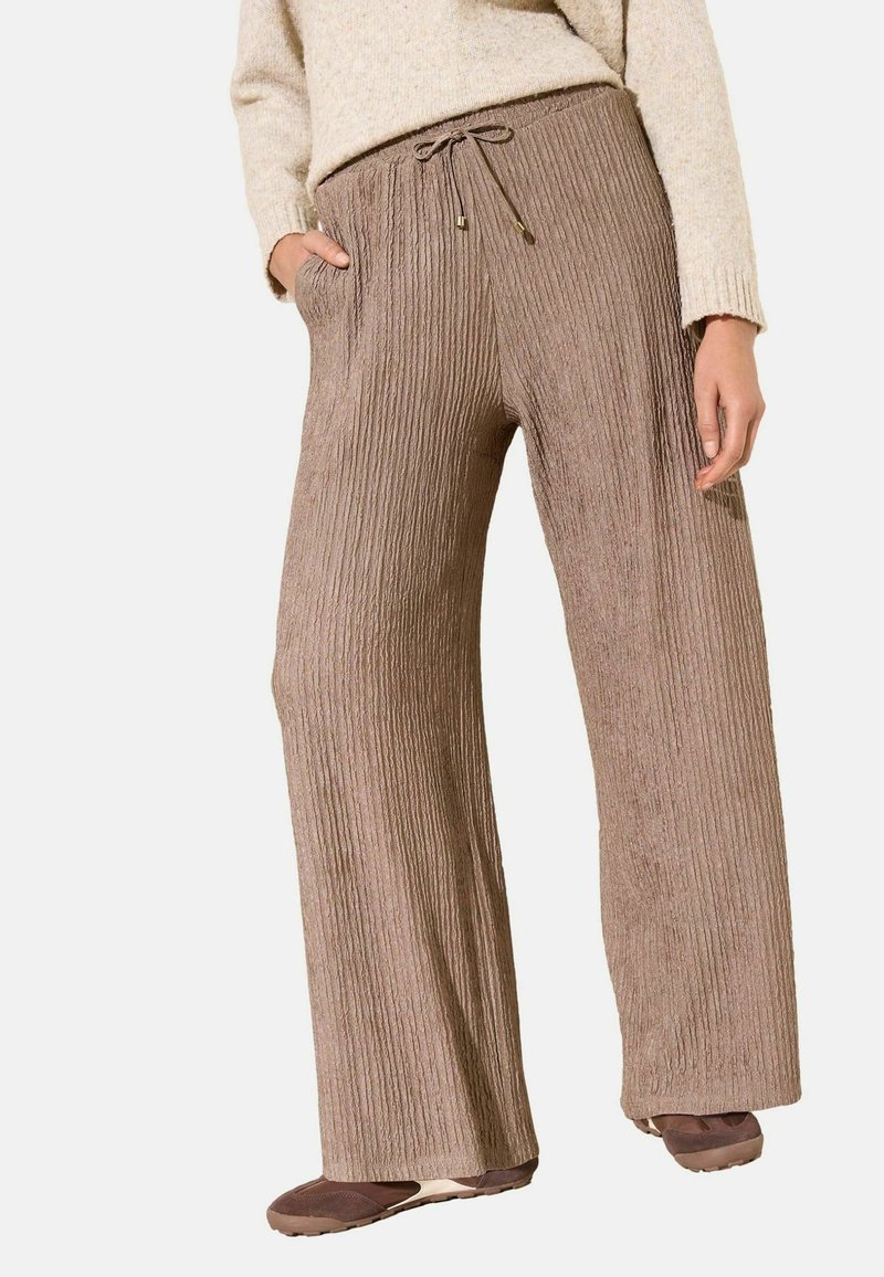 Püksid, mis on valmistatud soonikulisest, tekstuuriga pruunist kangast, millel on nööriga vöökoht ja küljetaskud, lahtise ja laiade sääreosade lõikega.