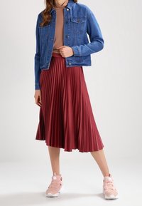 Giubbotto in denim, aderente con chiusura a bottoni, abbinato a una gonna midi plissettata bordeaux e scarpe da ginnastica rosa chiaro con suola bianca.