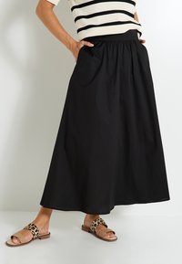 Falda negra hasta el tobillo con cintura fruncida y bolsillos laterales. Combinada con sandalias de estampado de leopardo y una blusa a rayas.
