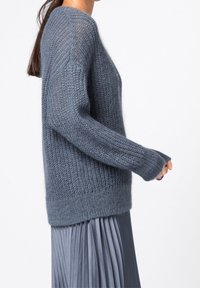 Pull léger en maille bleu gris doux avec une coupe ample. Présente des poignets et un ourlet côtelés. Les manches longues dépassent les poignets.