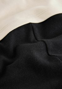Tela de algodón que presenta un suave color beige en la parte superior y un negro texturizado en la parte inferior. Los materiales están superpuestos con un detalle de costura visible.
