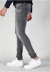 Jeans de mezclilla gris ajustados con detalles desgastados y una textura suave, combinados con zapatillas deportivas blancas.