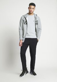 Szara bluza z zamkiem i czarnym logo, szara bluzka pod spodem, czarne slim-fit spodnie i czarne buty sportowe. Gładka tekstura, casualowy styl.