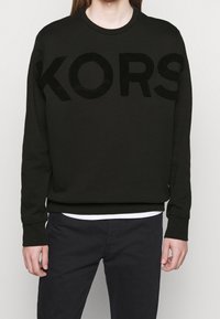 Sweatshirt nero con audace lettering "KORS" in rilievo sulla parte anteriore, dotato di colletto rotondo e polsini e orlo a costine.