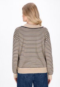Beżowy sweter w granatowe paski, o luźnym kroju, z ribbowanym kołnierzem i mankietami. Miękka tekstura z casualowym, sportowym designem.