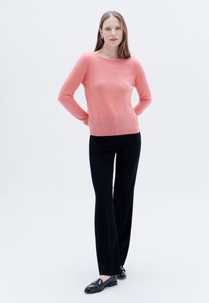 Pull en cachemire rose avec un col rond, associé à un pantalon noir ajusté et des mocassins noirs. Texture lisse et silhouette slim-fit.