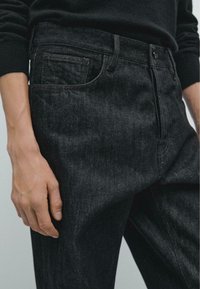 Jeans in denim scuro con una vestibilità rilassata, una textura sottile, design a cinque tasche e dettagli di cucitura a contrasto. Il tessuto sembra resistente.