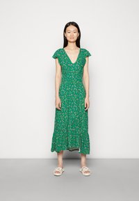Vestido floral verde com decote em V, mangas curtas com babados e saia em camadas. O tecido possui uma textura leve e está adornado com pequenas flores.