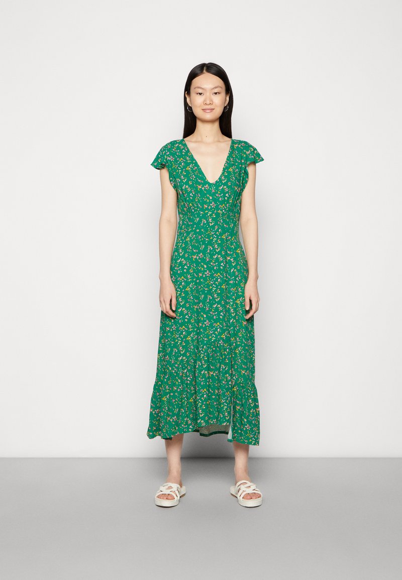 Vestido floral verde com decote em V, mangas curtas com babados e saia em camadas. O tecido possui uma textura leve e está adornado com pequenas flores.