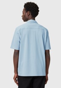 Camicia azzurra a maniche corte con colletto a punta, tessuto in cotone liscio e orlo dritto. La parte posteriore presenta un dettaglio di cucitura centrale.
