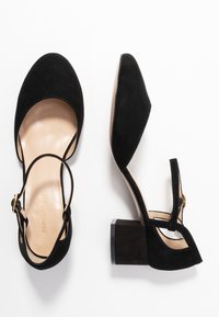 Zapatos de tacón alto de ante negro con puntera redondeada, correa al tobillo y tacón cuadrado. Presentan un forro interior suave y un sutil detalle del logo.