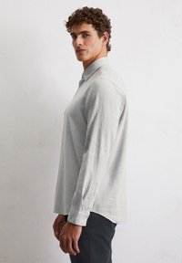 Chemise à manches longues gris clair avec col, fabriquée en tissu texturé, présentant une coupe droite et des détails de poignet à boutons.