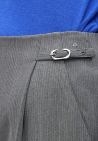 Šedé kalhoty s proužky a stříbrnou sponou na pásku. Látka má texturovaný vzhled, doplněné modrým topem pod nimi.