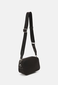 Borsa a tracolla nera di forma rettangolare, realizzata in un materiale liscio. Presenta una tracolla regolabile, hardware in argento e chiusura con zip.