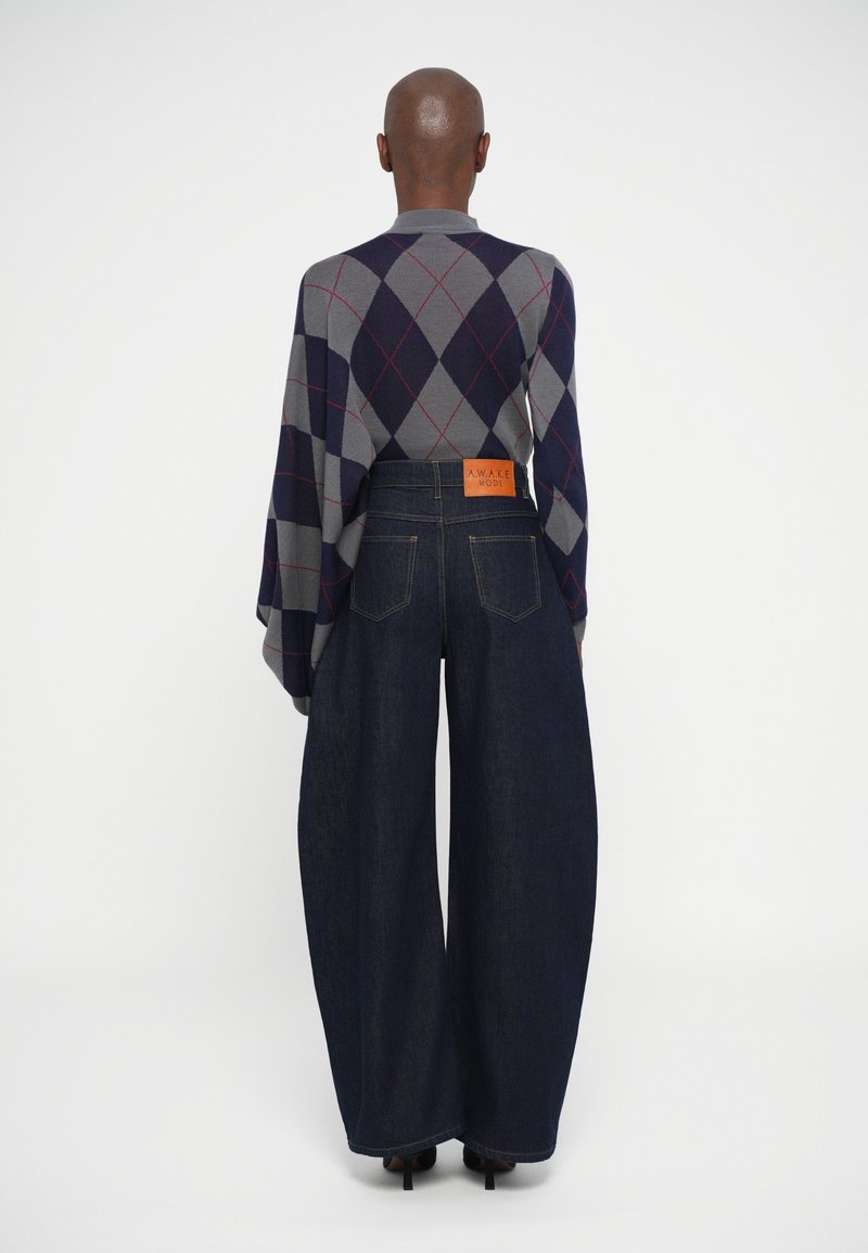 Persona vista da dietro che indossa un maglione argyle grigio e blu navy e un paio di jeans ampi di colore blu scuro con una toppa di pelle sulla vita.