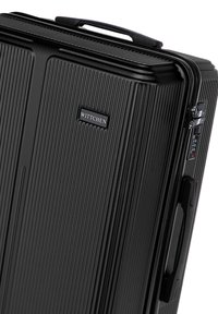Black hardshell suitcase with vertical ribbed texture, featuring a handle, TSA lock, and a subtle logo plate bearing "WITTCHEN."