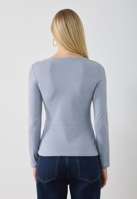 Long-sleeve top in light blue ribbed fabric, featuring a crew neckline and a smooth texture. Shown from the back with fitted design.