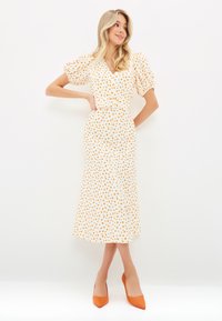 Abito midi bianco con pois gialli, maniche a sbuffo e scollatura a V. Abbinato a tacchi arancioni a punta. Tessuto morbido e vita aderente.