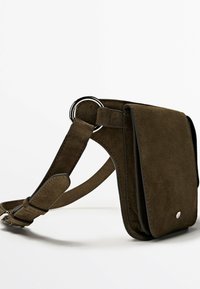 Sac bandoulière en daim vert olive avec fermeture à rabat, sangle réglable et détail de boucle anneau argenté.