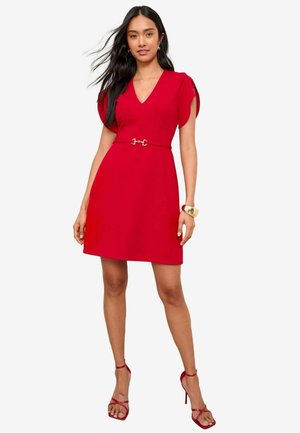 Rotes Kleid mit V-Ausschnitt, kurzen Ärmeln und einem Gürtel mit einer silbernen Schnalle. Glattes Gewebe und taillierte Silhouette. Accessoires sind Riemchen-Hochzeiten.