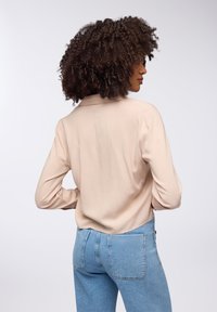 Camicia beige a maniche lunghe con colletto, tessuto liscio e vestibilità ampia, abbinata a jeans azzurri a vita alta con tasche posteriori.