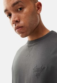 Gray sweatshirt featuring ribbed neckline, embroidered "Honesty Rules" logo on the chest, and subtle stitching detail. Smooth cotton texture.