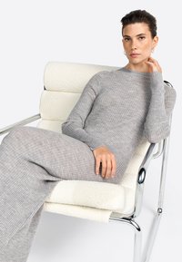 Gray ribbed knit dress with long sleeves, fitted silhouette, sitting on a white upholstered chair with chrome legs. Smooth, textured fabric.
