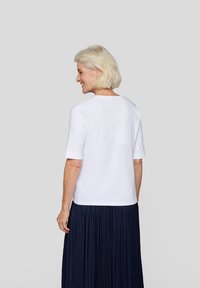Weißes Baumwoll-T-Shirt mit kurzen Ärmeln, runder Halsausschnitt und lockerer Passform, kombiniert mit einem marineblauen Faltenrock. Einfaches und sauberes Design.