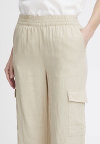 Pantalons en lin beige avec une taille élastique et des poches latérales, dotés d'une poche en applique sur la jambe pour plus de praticité.