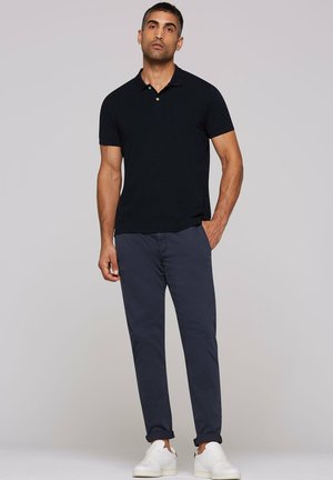 Schwarzes Poloshirt mit kurzen Ärmeln, kombiniert mit marineblauen Chinos. Weiße Sneakers. Einfaches und elegantes Design ohne sichtbare Muster oder Verzierungen.