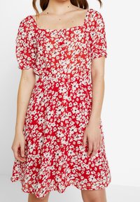 Rotes Blumenkleid mit kurzen, gepufften Ärmeln. Mit einem quadratischen Ausschnitt, einer durchgehenden Knopfleiste und einer taillierten Passform mit ausgestelltem Rock.