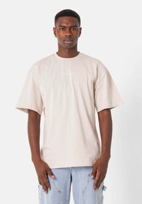 Lys beige bomulds t-shirt med korte ærmer, rund halsudskæring og et lille "Sixth June" logo trykt foran.