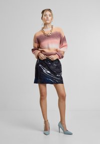 Gebreide trui in een roze en oranje gradient, gecombineerd met een zwarte glanzende mini-jurk. Accessoires omvatten een chunky gouden ketting en lichtblauwe hakken.