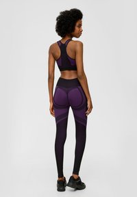 Lila und schwarze Sport-BH mit Racerback-Design, kombiniert mit hochtaillierten Leggings mit geschwungenen lila Akzenten und einer glatten Textur.
