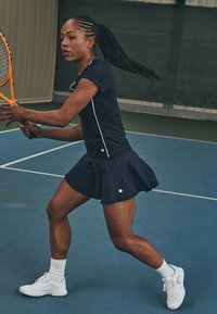 Tennis outfit with a fitted navy top and flared navy skirt. The player wears white athletic shoes and white ankle socks, holding an orange racket.