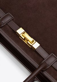 Bruine suède handtas met een gestructureerde afwerking, voorzien van gladde leren hengsels en een gouden metalen sluiting.