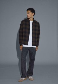 Geruite zwart en bruin flanellen overhemd over een witte crewneck t-shirt, gecombineerd met donkergrijze wijde jeans en lichtgrijze sneakers.