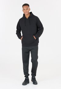 Svart huvtröja med framficka och snoddar, tillsammans med svarta avsmalnande byxor och svarta sneakers, allt i en enfärgad design.