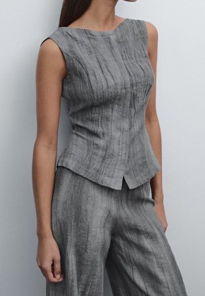 Femme portant un haut gris texturé sans manches avec de subtiles rayures verticales, associé à un pantalon large assorti, sur un fond uni.