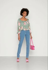 Blusa floral verde com mangas bufantes, jeans azuis, bolsa rosa e sandálias rosa de salto. Tecido suave, forma ajustada.