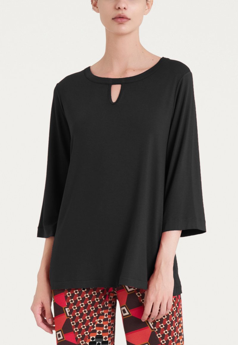 Top lungo nero, largo, con maniche lunghe e scollatura rotonda, caratterizzato da un dettaglio a occhio di chiave sul davanti. Tessuto liscio, design minimalista.