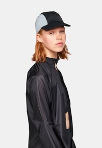 Svart lättviktsjacka med hög krage, tillsammans med en svart och grå tvåtonad cap. Capsen har en strukturerad skärm och textil med textur.