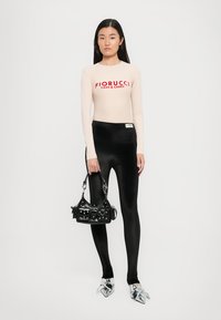 Fiorucci majica dugih rukava u svijetlo bež boji s crvenim logotipom, uparena s crnim sjajnim tajicama, crnom torbom i srebrnim cipelama s oštrim vrhom.